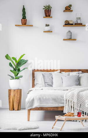 Plateau de petit-déjeuner debout sur le plancher à côté d'un grand lit confortable avec des draps, couvertures et oreillers dans une chambre blanche de l'intérieur. Photo réelle. Banque D'Images