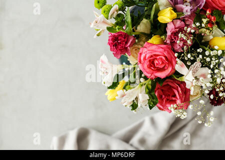 Vue de dessus d'un bouquet coloré de belles fleurs dans le coin et l'arrière-plan flou gris avec un morceau de tissu Banque D'Images