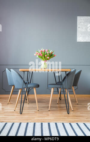 Tulipes fraîches en vase en verre debout sur table en épingle en bois gris à l'intérieur de salle à manger avec tapis Banque D'Images