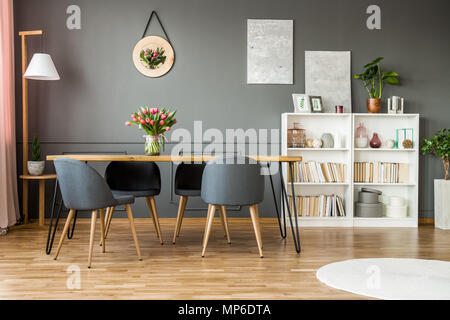 Rack en bois blanc avec des livres, le décor et les plantes fraîches debout dans la salle à manger gris intérieur avec des fleurs sur table en épingle Banque D'Images