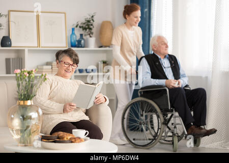 Smiling senior woman reading a book au cours de son séjour dans une maison de soins infirmiers Banque D'Images