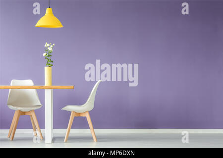 Un minimum d'intérieur avec deux chaises blanches, table avec une fleur dans un vase et une lampe de plafond jaune contre mur violet with copy space Banque D'Images