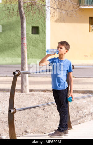 Garçon boit de l'eau d'une bouteille à l'extérieur. Banque D'Images