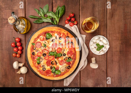 Photo prise à la verticale de la pizza au pepperoni, avec verre de vin blanc, huile d'olive, les feuilles de basilic, champignons, tomates cerises et mozzarellini fromage, tourné à partir de la société abo Banque D'Images