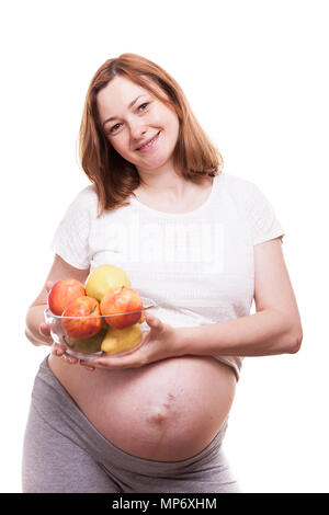 Femme enceinte en souriant à la caméra et tenant un bol en verre avec des fruits dans ses mains Banque D'Images