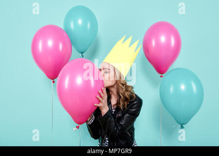 Magnifique jeune femme en blouson de cuir et party hat kissing balloon colorés, isolé sur fond de couleur bleu pastel. Concept d'anniversaire. Banque D'Images