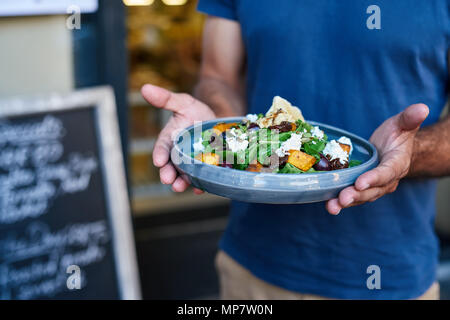 Homme tenant une délicieuse salade à la plaque d'un bistro Banque D'Images