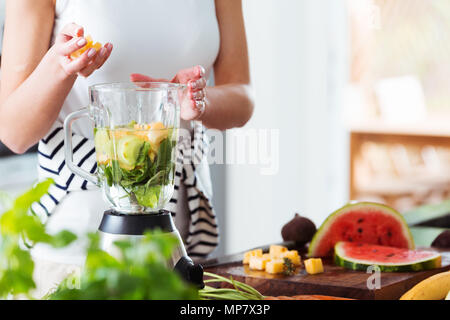 Woman throwing ananas en cubes dans un malaxeur avec de l'eau et de menthe smoothie énergétique lors de la préparation Banque D'Images