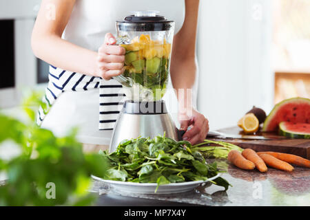 La préparation végétarienne smoothie vegan avec rucola, les agrumes, le concombre en cuisine avec comptoir de carottes Banque D'Images