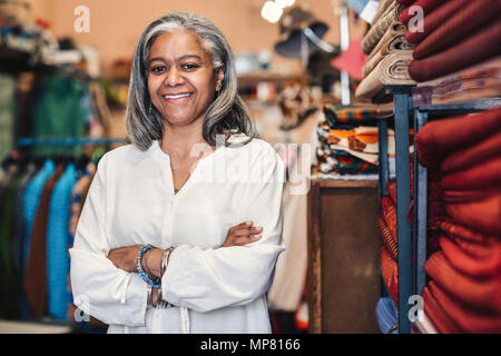 Smiling mature woman standing dans son magasin de tissus colorés Banque D'Images