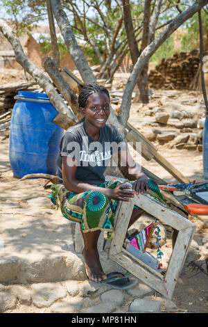 Femme africaine locale souriant de tresses, séance de travail à l'extérieur à l'échange, l'atelier créatif Katundu Likoma Island, le lac Malawi, Malawi, Afrique Banque D'Images