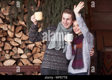 Photo de l'homme heureux et jolie femme avec des tasses en hiver en plein air. Maison de vacances d'hiver et vacances. Christmas couple heureux de l'homme et la femme boire du café chaud. Bonjour amis Banque D'Images