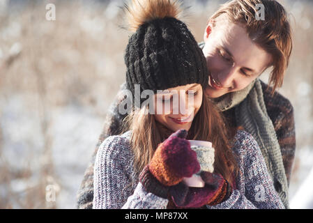 Photo de l'homme heureux et jolie femme avec des tasses en hiver en plein air. Maison de vacances d'hiver et vacances. Christmas couple heureux de l'homme et la femme boire du vin chaud. Couple in love Banque D'Images