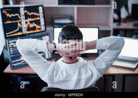 L'élaboration de nouvelles approches. Vue arrière du jeune homme dans des vêtements décontractés holding hand sur l'arrière de la tête et de travail tout en étant assis au bureau dans creative office Banque D'Images