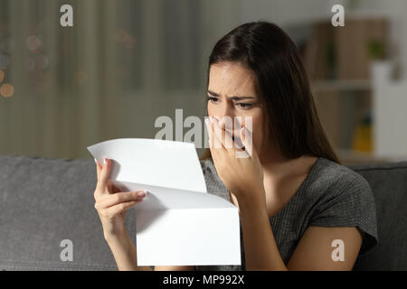 Femme triste de se plaindre la lecture d'une lettre dans la nuit, assis sur un canapé dans la salle de séjour à la maison Banque D'Images