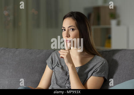 Femme pour demander le silence avec le doigt sur les lèvres de la nuit assis sur un canapé dans la salle de séjour à la maison Banque D'Images