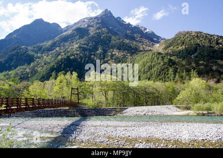 Un pont suspendu traverse la rivière dans la région Kamikochi des Alpes Japonaises, Nagano, avec parmi les arbres verdoyants et de hautes montagnes dans l'arrière-plan Banque D'Images