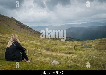 Une femme regarde à travers le paysage de la Cumbrie roulant haut de Honister Pass, alors que des nuages gris forme devant nous. Banque D'Images