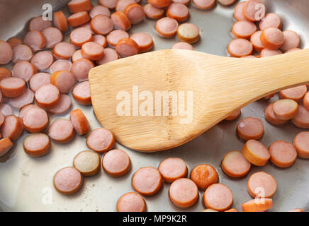 Vue latérale des tranches de saucisson fumé cuit dans une poêle avec une cuillère en bois. Banque D'Images