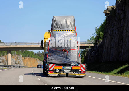 Semi-remorque jaune avec un objet industriel comme charge va passer sous un pont d'autoroute sur une journée ensoleillée en Finlande, Paimio - 18 mai, 2018. Banque D'Images