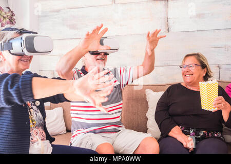 Trois cadres supérieurs d'essayer la technologie de la réalité virtuelle à la maison. Assis sur le canapé sourire et rire pour la nouvelle expérience au moment de la retraite. Concept d'amitié Banque D'Images
