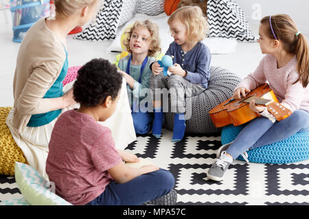 Groupe d'enfants d'âge préscolaire assis sur un tapis à la maternelle Banque D'Images