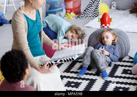 Groupe d'enfants allongés sur un tapis pendant la lecture à la maternelle Banque D'Images