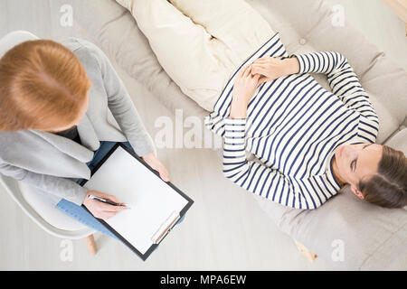 Concept de psychothérapie, thérapeute de prendre des notes tandis que les femmes le patient est couché sur la table et de parler Banque D'Images