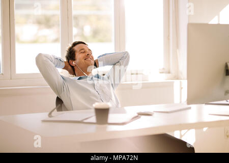 Smiling businessman relaxing at home assis devant sa table de travail. L'homme de faire une pause et d'écoute de musique à l'aide d'écouteurs avec les yeux fermés. Banque D'Images