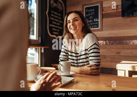 Smiling woman sitting in a restaurant parler à son ami. Amis assis dans un café avec du café et des collations sur la table. Banque D'Images