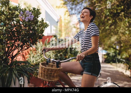 Cheerful woman avec son vélo de rire à l'extérieur. La femme un vélo dans la ville. Banque D'Images