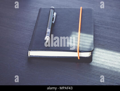 Close up black bloc-notes avec crayon mécanique moderne sur table en bois noir avec la lumière du soleil à partir de la fenêtre,office d'alimentation. Banque D'Images