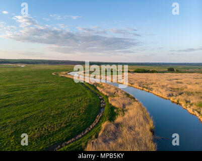 Ruisseau serpente au milieu de champs verts et de prairies au coucher du soleil. Beau paysage avec une vue d'un soir d'été Banque D'Images