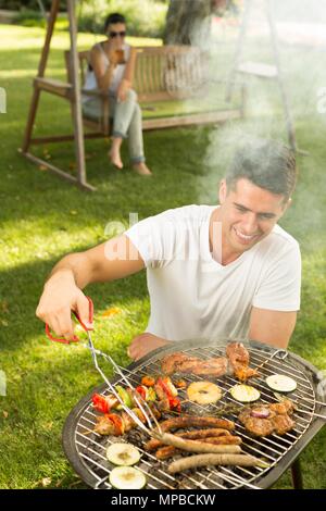 Jeune homme griller les saucisses sur le barbecue Banque D'Images