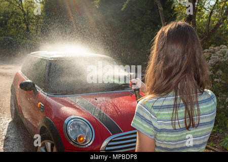 Une femme dans la quarantaine laver sa voiture dans le soleil. Banque D'Images