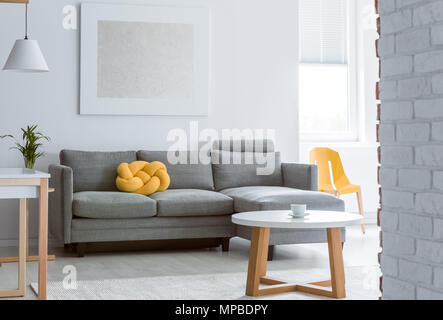 Coussin déco jaune gris sur canapé dans salon avec mur de brique et blanc simple table basse Banque D'Images