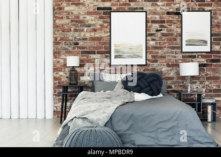 Nœud noir oreiller placé sur un lit avec literie gris dans cette chambre élégante avec des affiches pendaison sur mur de brique Banque D'Images