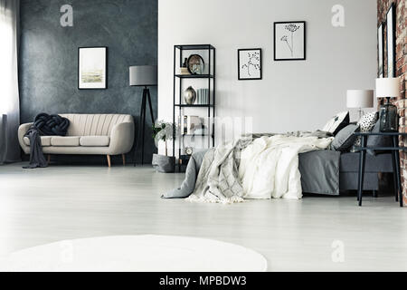 Spacieuse, cette chambre avec gris multifonctions canapé beige contre mur en béton et des dessins sur mur blanc Banque D'Images