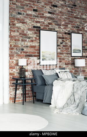 Deux affiches accroché sur un mur de briques dans une chambre de style loft avec lampe sur table de chevet Banque D'Images
