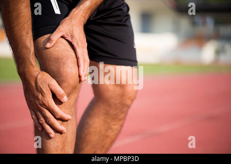 Lésions du genou. Les jeunes sport homme avec de fortes jambes athlétiques tenant le genou avec ses mains dans la douleur après avoir subi une lésion musculaire au cours d'une séance d'entraînement en marche tr Banque D'Images