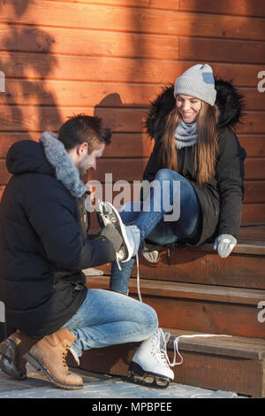 Homme aidant une femme heureuse à porter des patins à glace sur les marches Banque D'Images