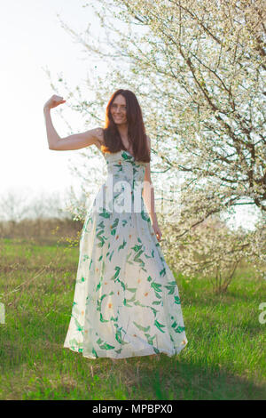 Sportive mince brun aux yeux bleus dans un jardin fleuri en pleine croissance au soleil montre une forte biceps Banque D'Images