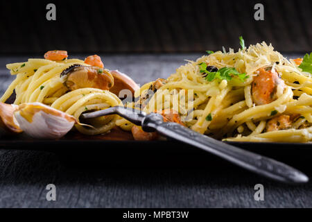 Pâtes aux crevettes fruits de mer et les moules en sauce crémeuse sur une plaque sur un fond sombre Banque D'Images