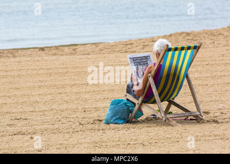 Bournemouth, Dorset, UK. 22 mai 2018. Météo France : après un couvert nuageux pour la journée, le soleil revient et les visiteurs chef à la plage pour profiter du soleil. Femme lit journal en transat. Credit : Carolyn Jenkins/Alamy Live News Banque D'Images