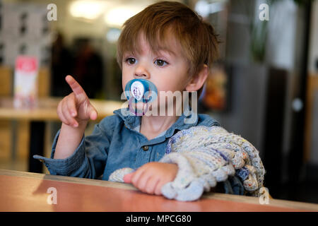 18 mois du garçon est assis dans une chaise haute avec mannequin et couverture confort Banque D'Images