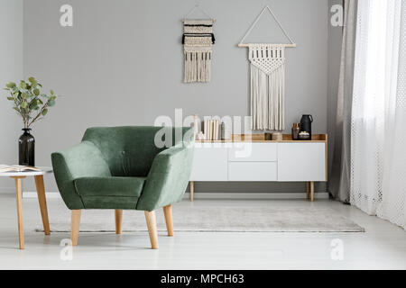 Fauteuil vert lumineux salon boho en intérieur avec des plantes sur table et décor sur le mur. Photo réelle Banque D'Images