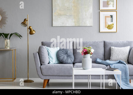 Lampe d'or à côté de gray canapé dans salon moderne avec intérieur affiche sur un mur. Photo réelle Banque D'Images