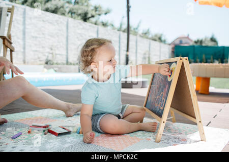 Un enfant en s'appuyant sur un tableau noir et apprendre à lire l'heure. A smiling little boy le temps d'apprentissage avec sa maman à la maison. Banque D'Images