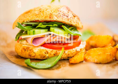 Burger de jambon ou un sandwich avec des tranches de jambon, fromage, concombres, tomates et de la laitue avec des quartiers de pommes de terre, maison rustique sandwich Banque D'Images