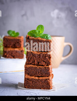 Pile de tranches de carrés brownie au four sur une feuille de papier, derrière un arrière-plan flou gris Banque D'Images